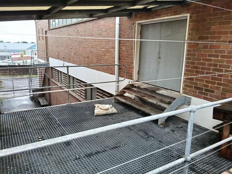 Industrial rear exterior area featuring a metal grating platform, safety railings, and a metal staircase leading to a double door entrance.