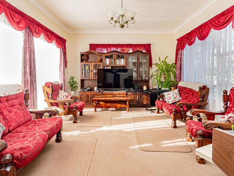 A spacious living room featuring classic architectural details including a central ceiling rose, chandelier, and decorative cornice work.