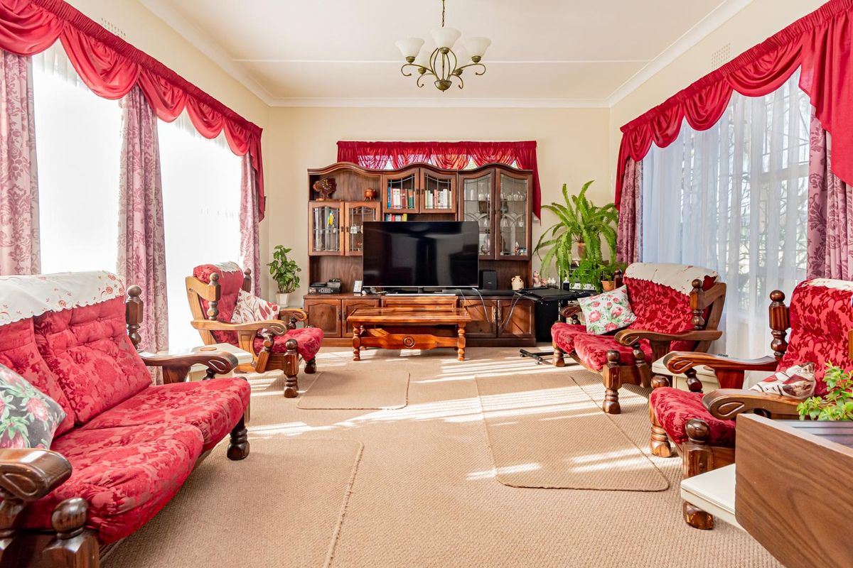 A spacious living room featuring classic architectural details including a central ceiling rose, chandelier, and decorative cornice work.