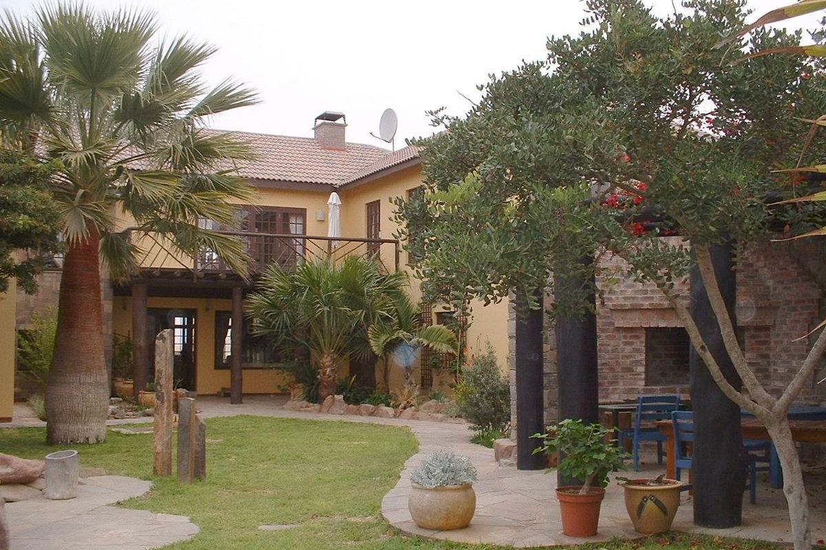 A spacious rear garden featuring a paved patio area, built-in brick fireplace, and a two-story house with a balcony and tiled roof.
