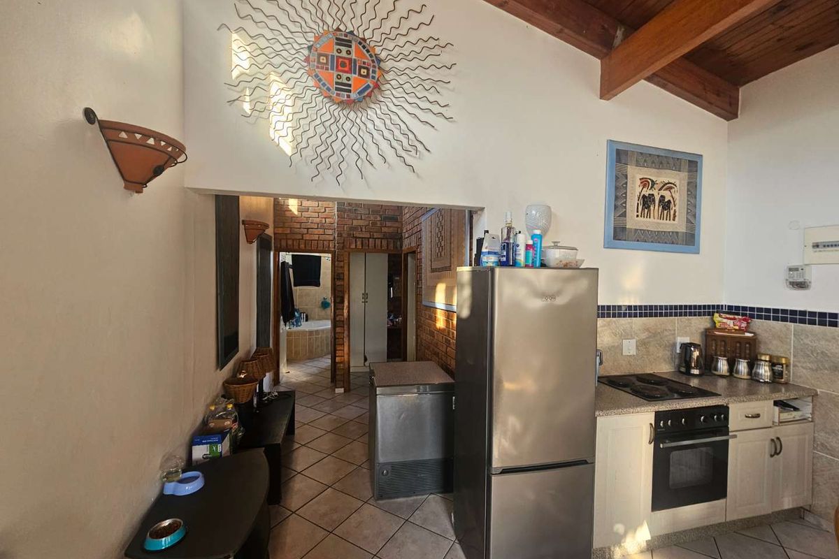 A kitchen area featuring tiled flooring, built-in cabinetry, and an integrated oven and hob, leading into a hallway with exposed brickwork.