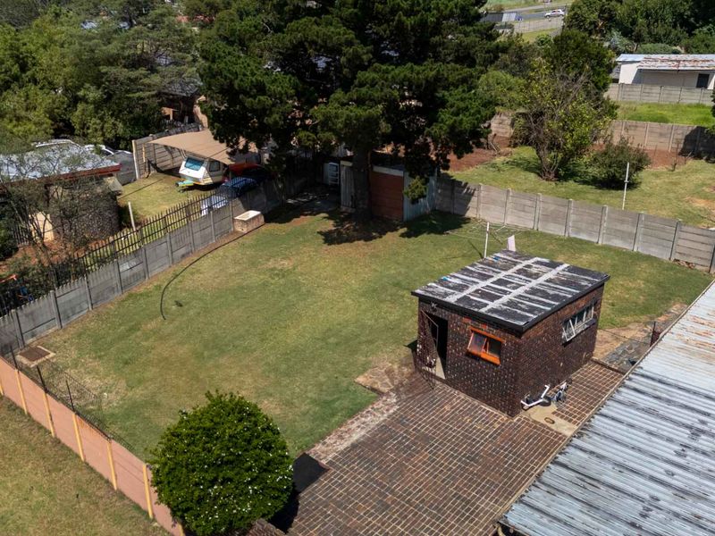 Aerial view of a spacious backyard featuring a large lawn, mature trees, a brick outbuilding, and a paved patio area enclosed by boundary walls.