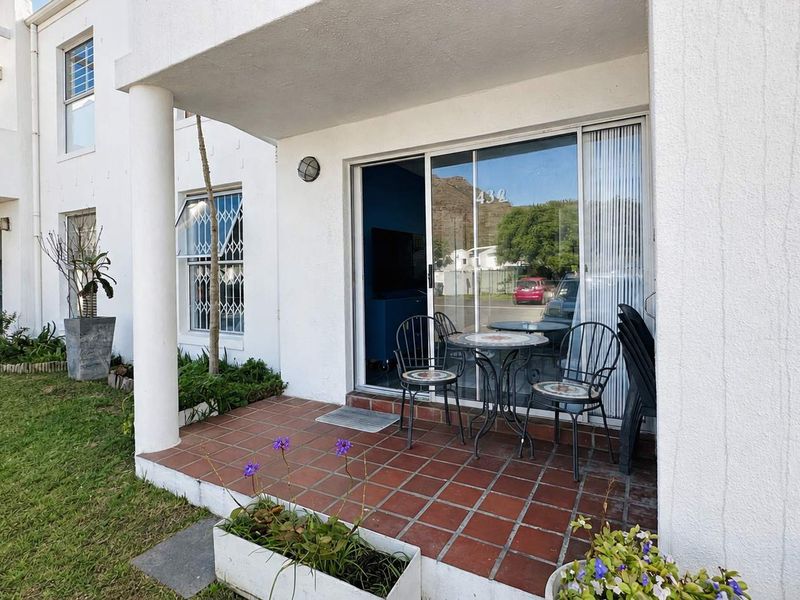 A covered ground-floor patio featuring terracotta tiling, a sliding glass door entrance, and direct access to the communal garden area.
