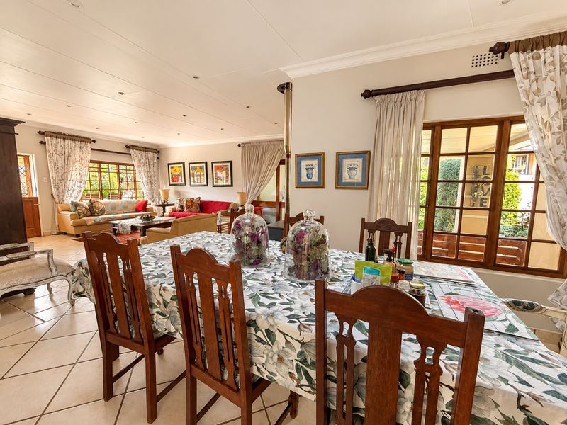 Spacious open-plan living and dining area featuring tiled flooring, recessed lighting, and large wooden-framed glass doors providing natural light and garden access.