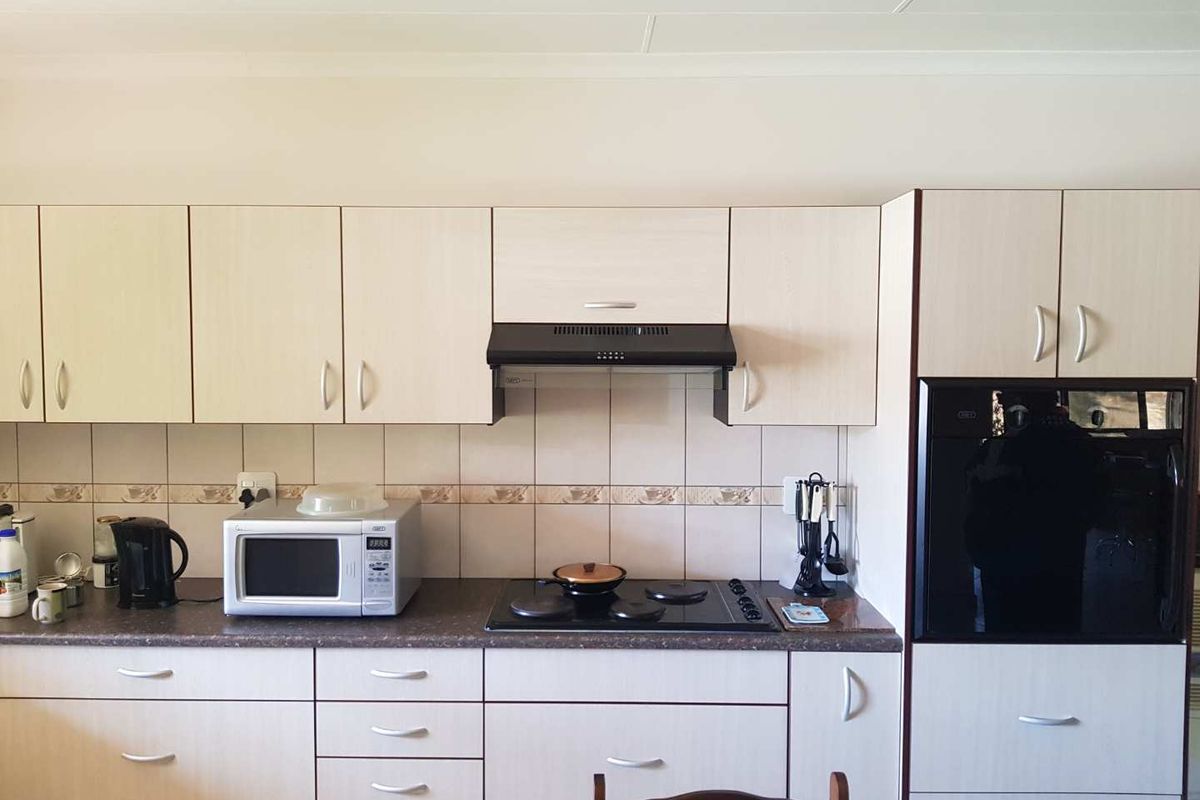 A functional kitchen featuring light-toned cabinetry, a built-in oven, a black electric hob, and a matching extractor fan with tiled splashbacks.