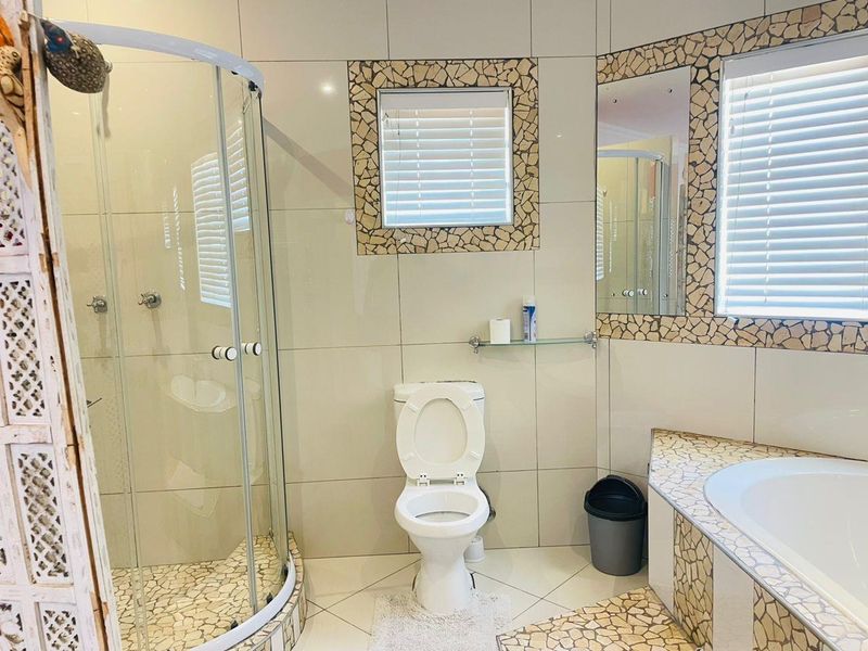 A functional bathroom featuring a curved glass shower, built-in bathtub, and decorative mosaic tile accents around the windows and tub surround.