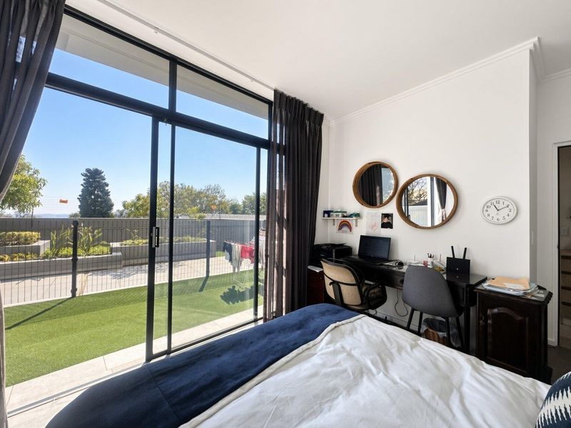 Bright bedroom featuring large sliding glass doors that open onto a private balcony with artificial turf and outdoor views.