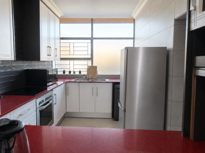 Modern kitchen featuring contrasting black and white cabinetry, vibrant red countertops, integrated appliances, and large windows providing ample natural light.