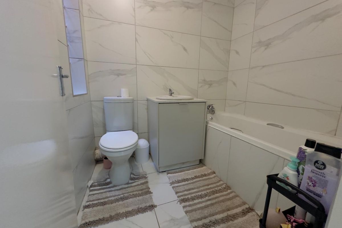 A modern bathroom featuring floor-to-ceiling marble-look wall tiles, a built-in bathtub, a vanity cabinet with a basin, and a standard toilet.