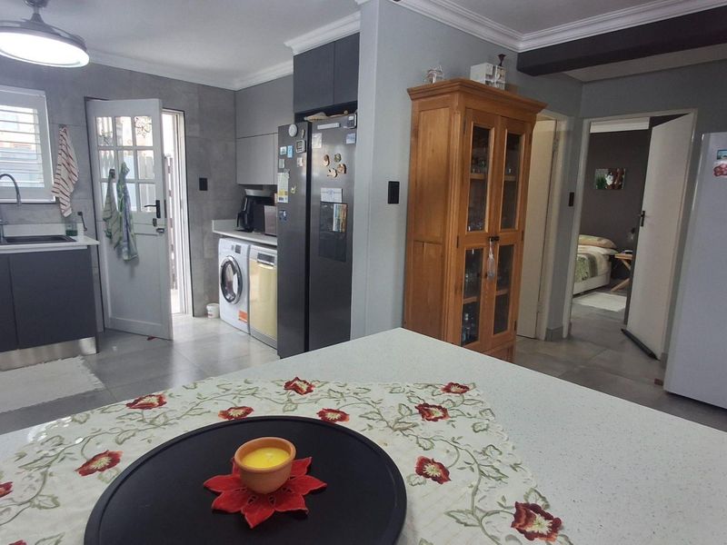 A functional kitchen featuring modern grey cabinetry, stone countertops, an undermount sink, and integrated laundry facilities with tiled flooring throughout.