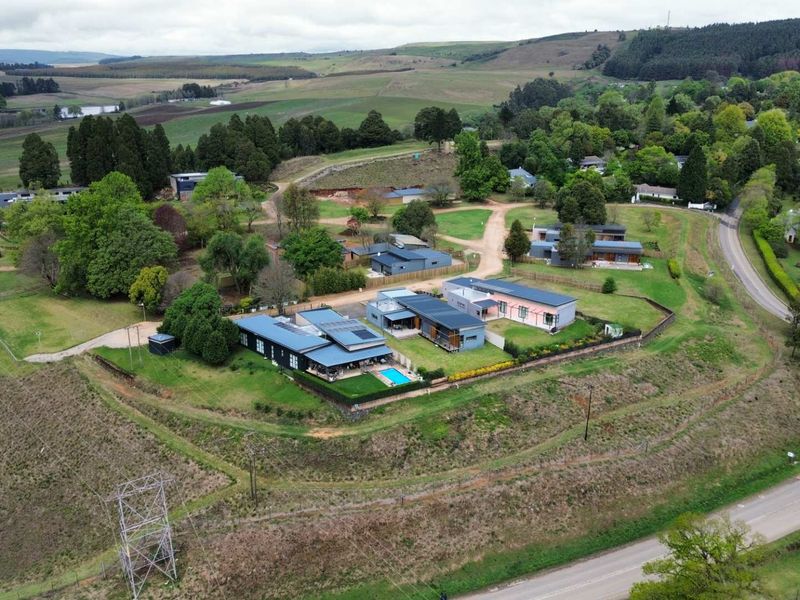 An aerial view of a residential property featuring multiple buildings, a swimming pool, and landscaped grounds set within a rural landscape.