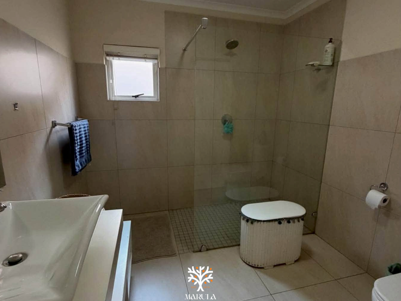 Modern bathroom featuring a spacious walk-in shower with glass screen, vanity basin, and neutral floor-to-ceiling tiling.