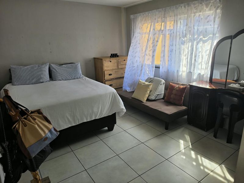 A bedroom featuring tiled flooring and a large window with natural light, providing a functional space with potential for cosmetic updates.