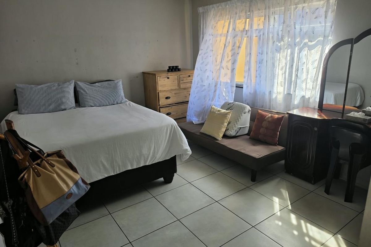 A bedroom featuring tiled flooring and a large window with natural light, providing a functional space with potential for cosmetic updates.