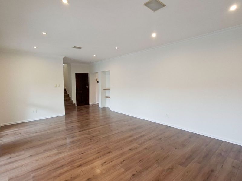 A spacious, empty living area featuring modern laminate flooring, recessed lighting, and a staircase leading to the upper level.