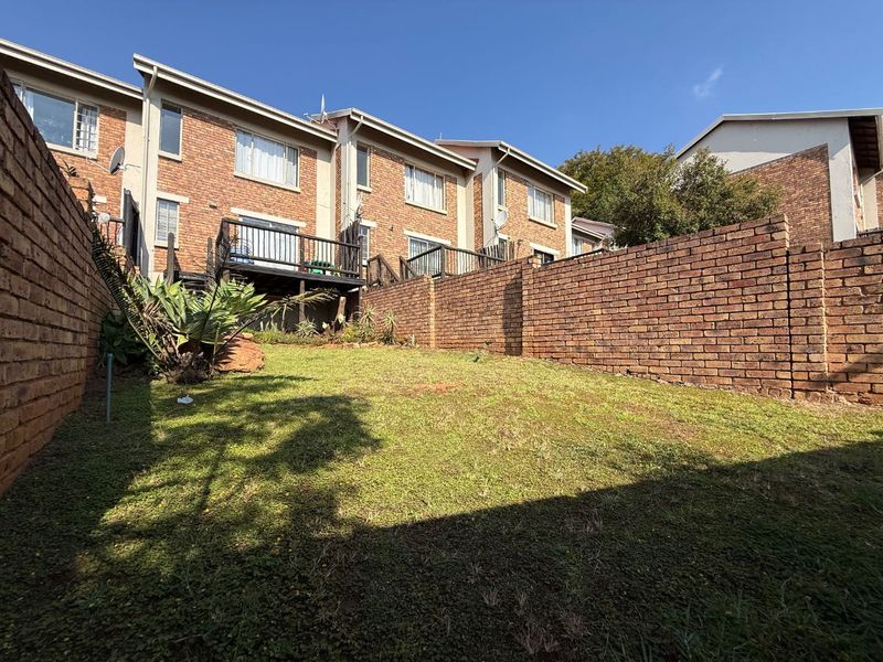 Rear view of the townhouse featuring a private garden, brick boundary walls, and an elevated timber deck accessible from the main living area.