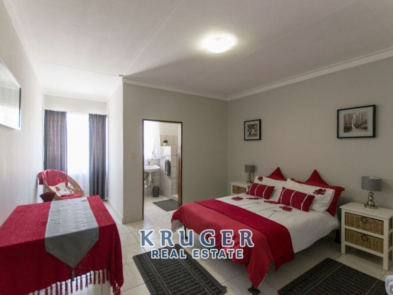 A spacious bedroom featuring tiled flooring, neutral wall finishes, and an en-suite bathroom access point.