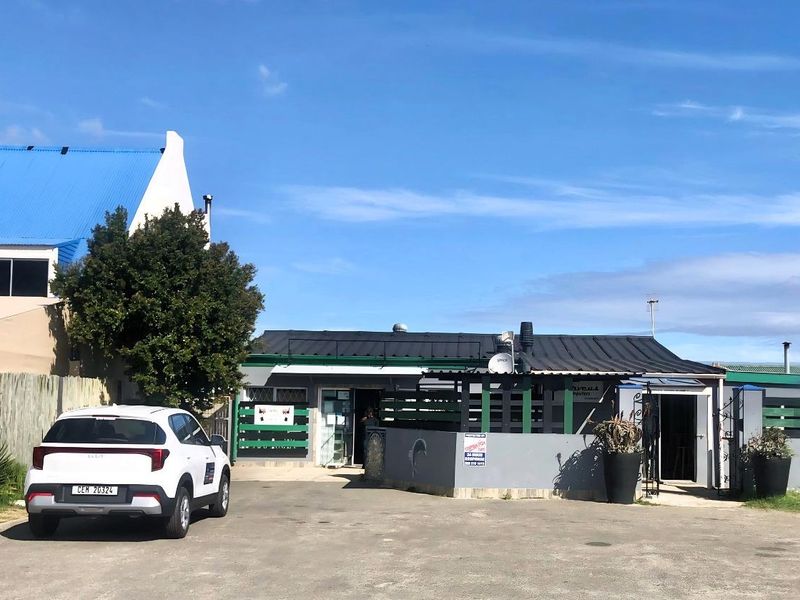 Front exterior view of a commercial property featuring a paved driveway, boundary wall, and metal roofing.