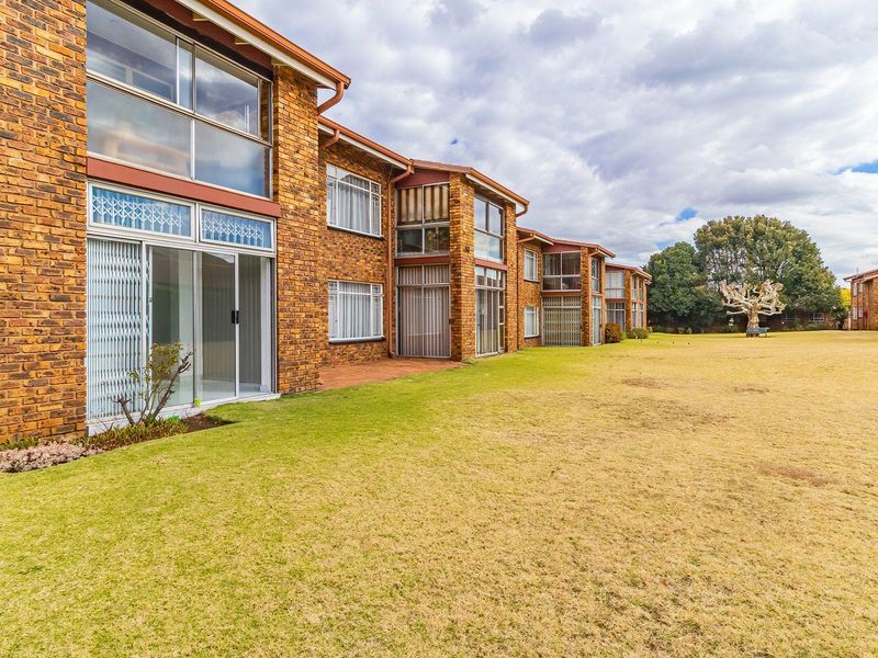 Rear view of a face brick townhouse complex featuring large windows, sliding glass doors, and a spacious communal lawn area.