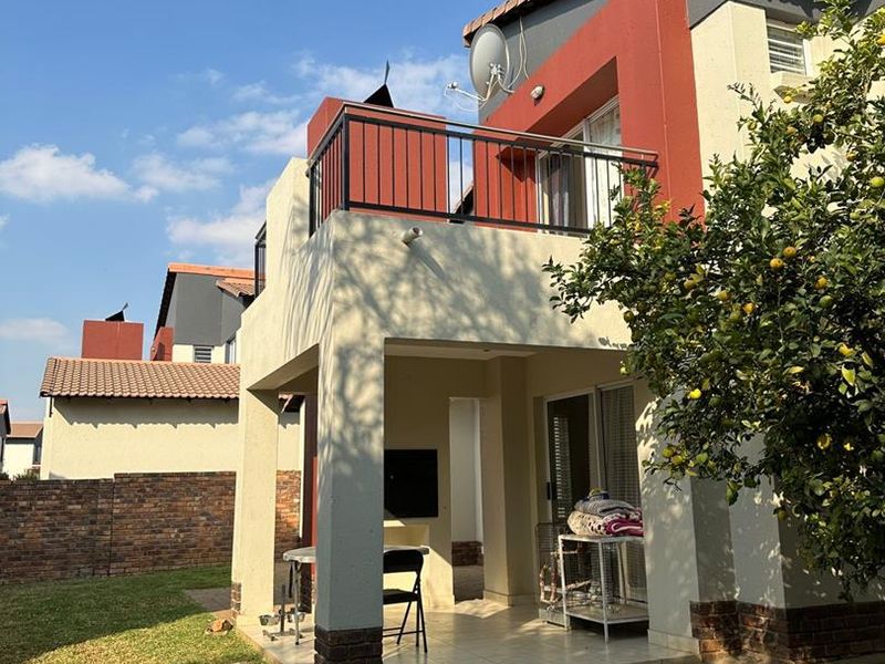 Rear view of the property featuring a covered patio with a built-in braai, an upper-level balcony, and a private garden area.