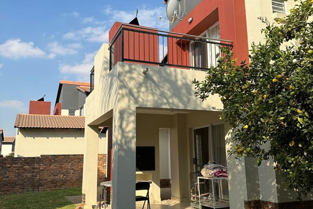 Rear view of the property featuring a covered patio with a built-in braai, an upper-level balcony, and a private garden area.