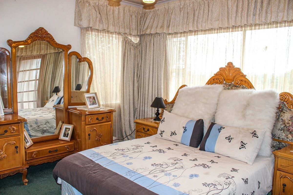 A bedroom featuring large windows with floor-to-ceiling curtains and carpeted flooring.