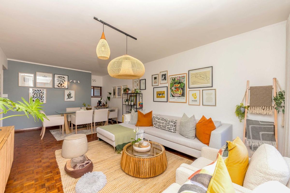 A bright and inviting open-plan living and dining area featuring warm parquet flooring, a stylish accent wall, and modern pendant lighting.