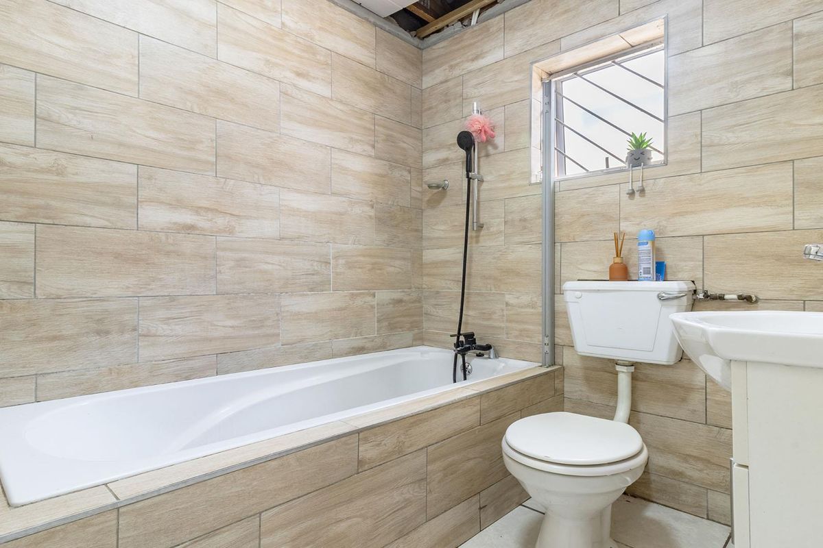 A bathroom featuring wood-look wall tiles, a bathtub with a handheld shower attachment, a standard toilet, and a pedestal basin.