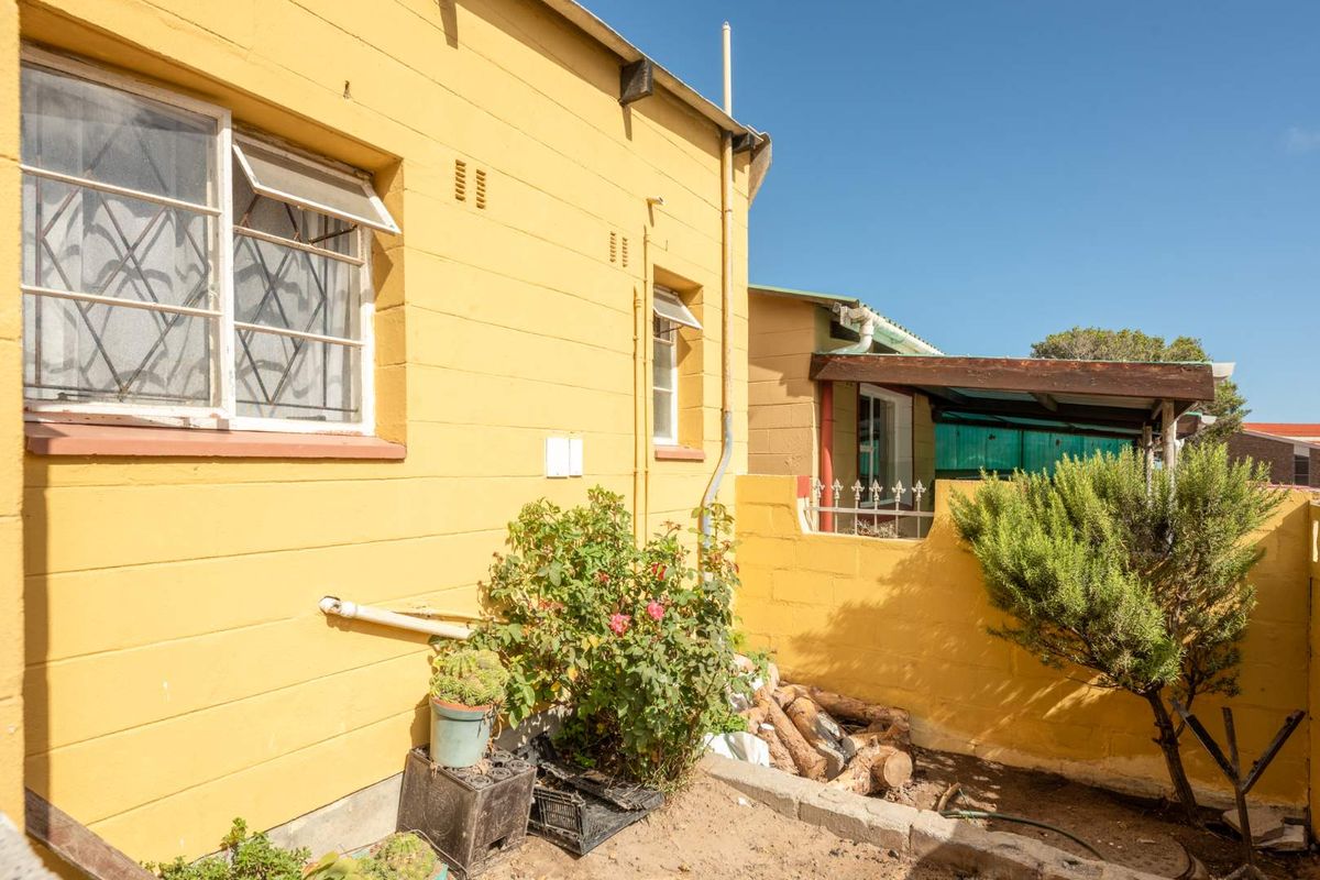 A view of the rear exterior of the property featuring yellow painted masonry walls, security-barred windows, and a small paved courtyard area.