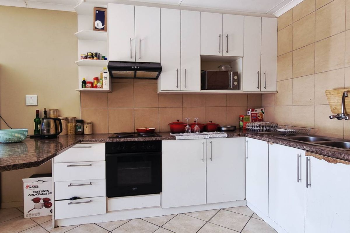 A functional kitchen featuring white cabinetry, a dark laminate countertop, built-in oven, extractor fan, and a double stainless steel sink.