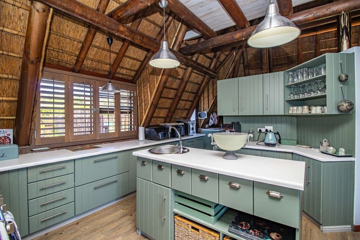 A charming kitchen featuring sage green cabinetry, a central island with a sink, and a distinctive exposed thatch roof with timber beams.