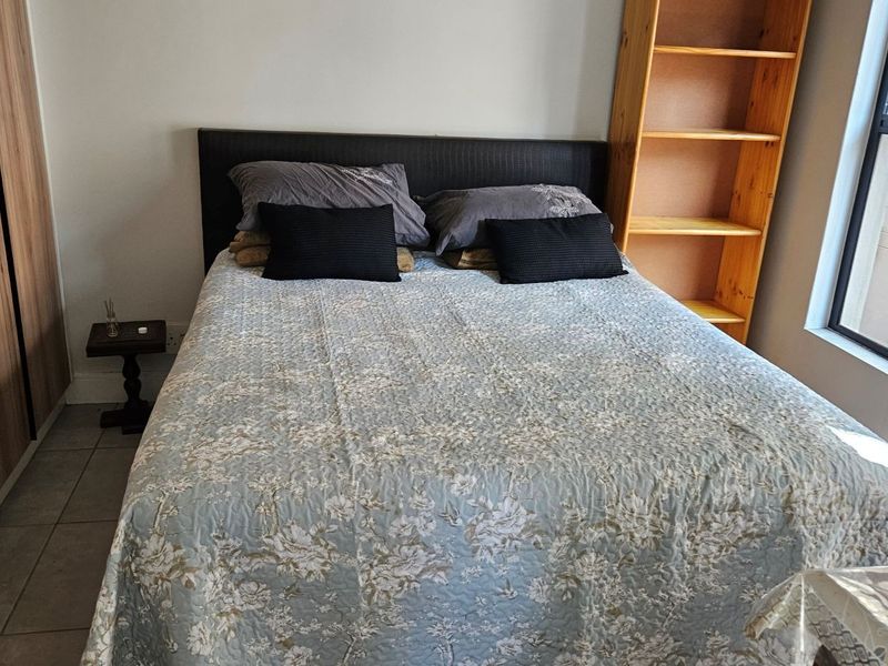 A functional bedroom featuring built-in wardrobes, tiled flooring, and natural light from an aluminium-framed window.