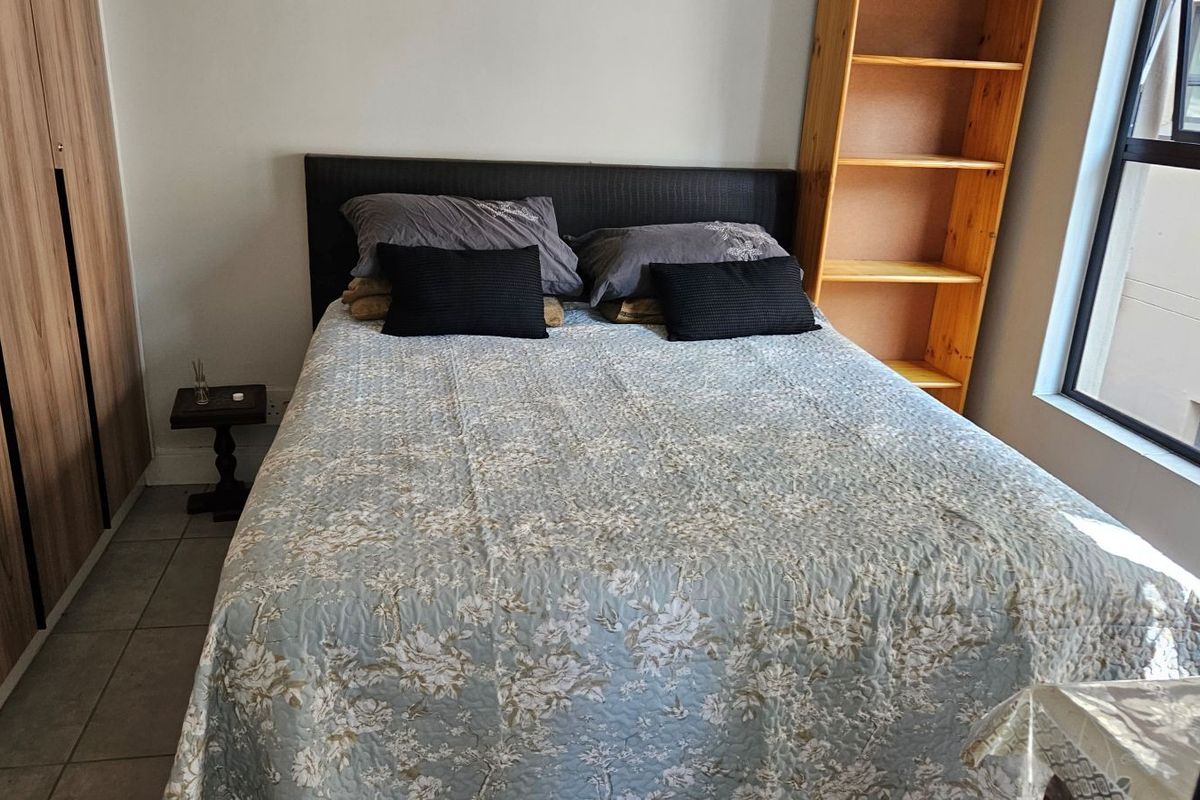 A functional bedroom featuring built-in wardrobes, tiled flooring, and natural light from an aluminium-framed window.