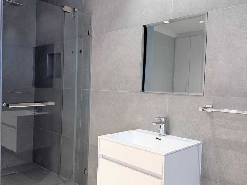 Modern bathroom featuring a wall-mounted vanity, glass shower enclosure with rain shower head, and contemporary grey tiling throughout.