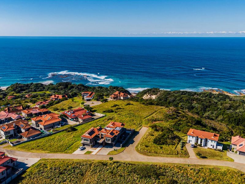 An aerial view of a coastal residential estate featuring multiple homes with tiled roofs, solar panels, and paved access roads overlooking the ocean.