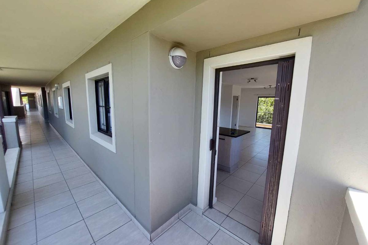 View of an apartment entrance from a tiled exterior walkway, showing a secure door leading into an open-plan living area.