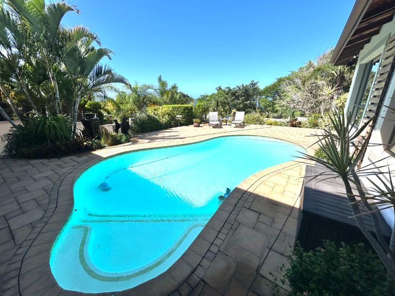 A well-maintained swimming pool area featuring a paved deck, lush surrounding garden, and clear blue water, perfect for outdoor relaxation.