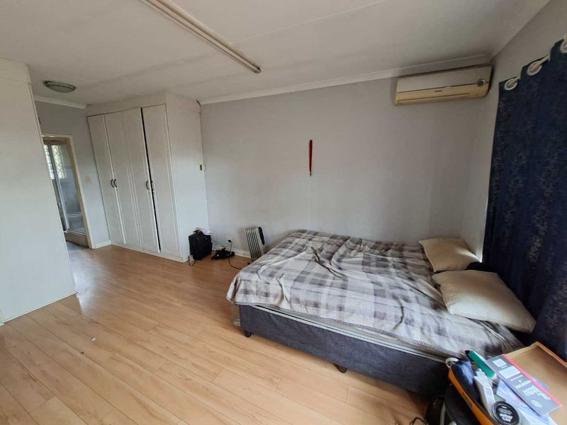A bedroom featuring laminate flooring, built-in cupboards, and a wall-mounted air conditioning unit.