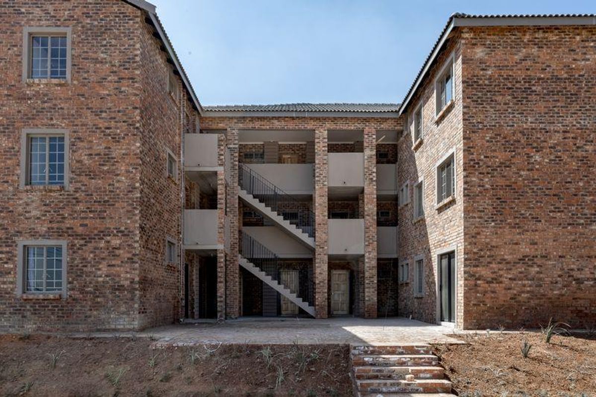 Rear view of a multi-story apartment building featuring face brick construction, external staircases, and a paved ground-level patio area.