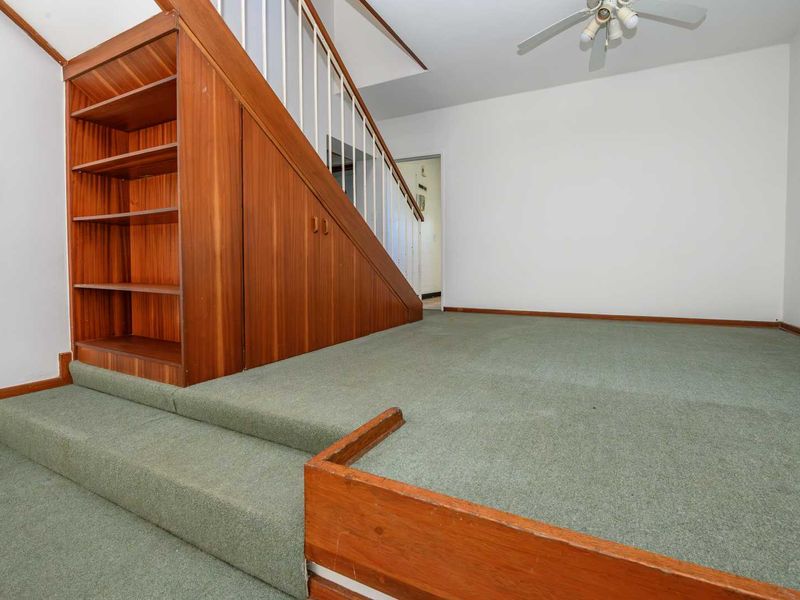 An empty living area featuring a built-in wooden staircase with integrated storage shelving and carpeted flooring.