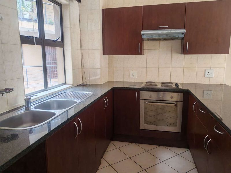 A functional kitchen featuring dark wood cabinetry, granite countertops, a built-in oven with hob, and a double sink with tiled splashbacks.