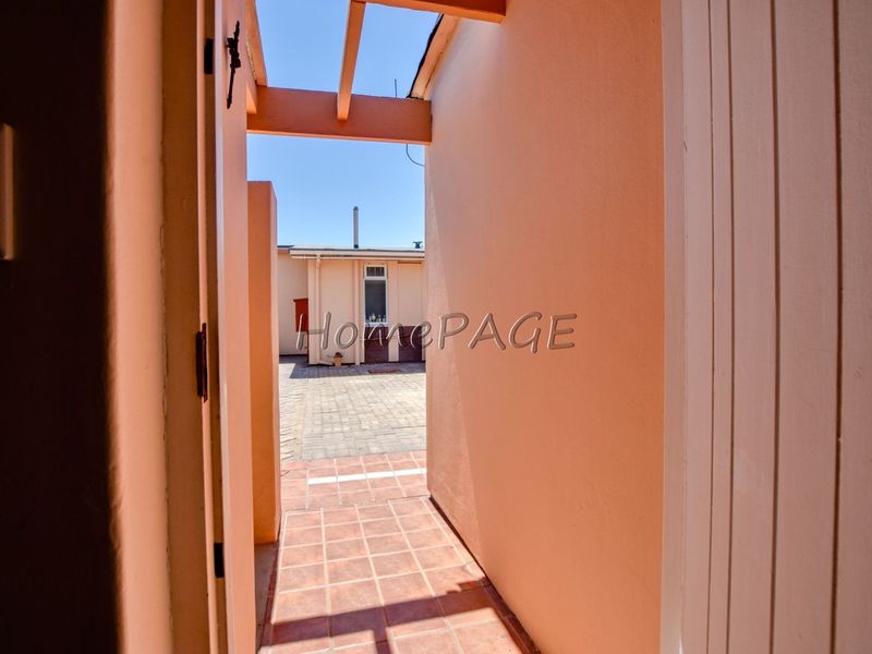 A covered outdoor walkway featuring tiled flooring and a timber pergola, leading to a paved rear courtyard area.