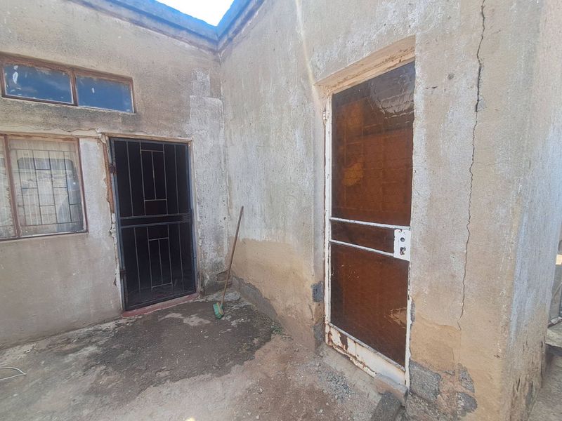 Rear exterior view of the property showing weathered walls, security gates, and concrete paving requiring maintenance and repair.