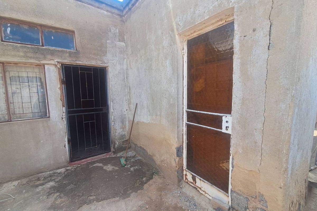 Rear exterior view of the property showing weathered walls, security gates, and concrete paving requiring maintenance and repair.
