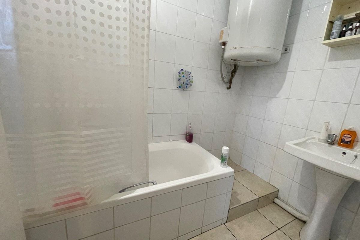 A functional bathroom featuring a tiled bathtub with shower curtain, pedestal sink, and a wall-mounted electric water heater.