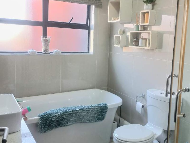 A modern bathroom featuring a freestanding bathtub, a separate shower enclosure, a toilet, and a vanity with a basin, finished with neutral wall tiles.