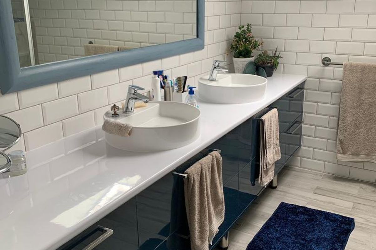 Modern bathroom featuring a double vanity with vessel sinks, high-gloss cabinetry, subway tile backsplash, and dual skylights providing ample natural light.
