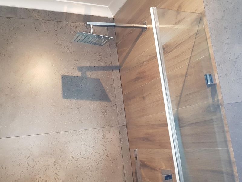 A modern shower enclosure featuring a contemporary rain shower head, glass screen, and a stylish combination of grey stone-look and wood-look wall tiles.