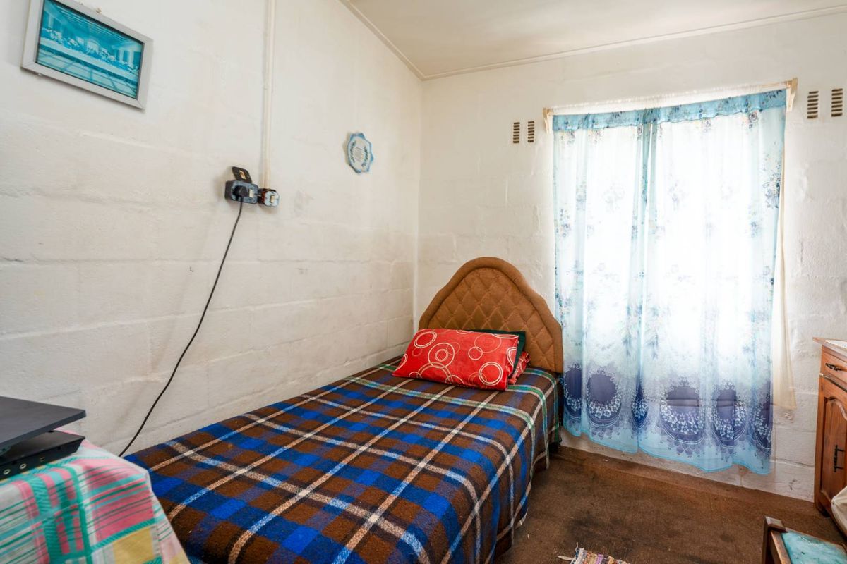 A compact bedroom featuring exposed blockwork walls, a single window with curtaining, and basic electrical fixtures.