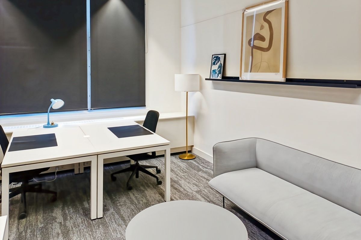 A modern, well-lit office space featuring neutral tones, carpeted flooring, roller blinds, and a clean, professional layout suitable for a productive work environment.